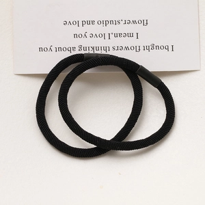Detail of two high-elasticity black hair ties with reinforced joints on aesthetic white paper