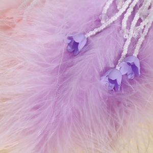Vue macro d'un charme en perles de muguet avec fleurs mauves sur plumes douces