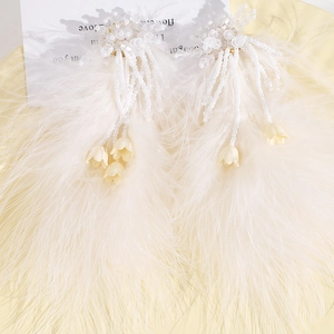 Détail de boucles d'oreilles en plumes d'autruche blanches avec perles et fleurs