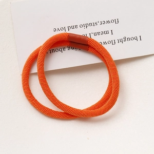 Detail view of two bright orange braided elastic hair ties with seamless brown connectors