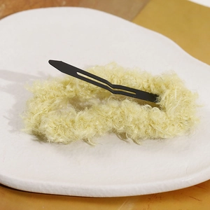 Fuzzy light yellow plush hair clip with black metal snap closure on a textured white tray