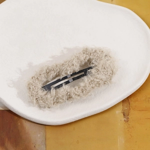 Close-up of beige plush faux lamb wool covered BB hair clip on a ceramic tray