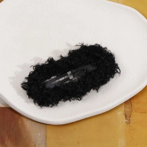 Close-up of a black plush BB hair clip with fluffy texture on a white decorative tray