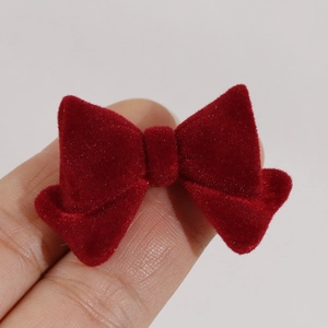 Macro shot of a mini red flocked bow tie accessory held between fingers for size