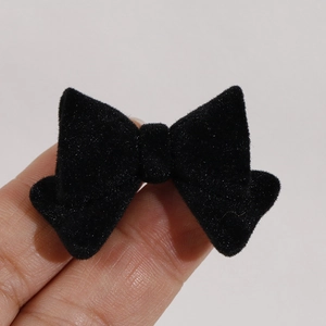 Close-up of a small black flocked bow resin charm held by fingers for DIY hair accessories