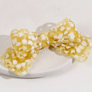 Chic acetate bow hair clip with yellow and white floral pattern on a stone display