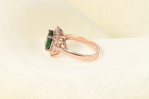 Macro di anello in oro rosa con smeraldo ovale e alone di zirconi brillanti di contorno