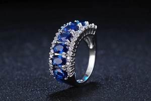 Macro shot of silver ring featuring five oval blue sapphires with double row pave diamonds
