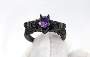 Macro detail of gothic bat ring in black metal with purple zircon held in white gloves