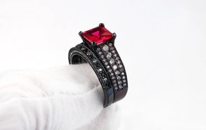 Detail of black gold ring set with princess cut red gemstone and pavé white zircons