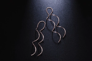 Dettaglio di orecchini a onde oro rosa con finitura lucida su sfondo nero opaco