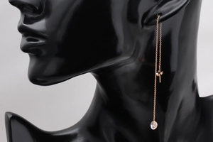 Dettaglio di orecchini passanti oro rosa con croce e pendente in zircone a goccia