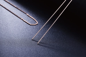 Dettaglio macro di orecchini a onde in oro rosa con sottili maglie in metallo lucido