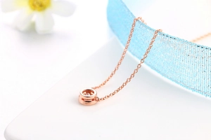 Vista macro di una collana in oro rosa con ciondolo tondo in zircone e sottile catena a maglie
