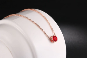 Dettaglio della collana in oro rosa con pendente in zircone rosso su ceramica bianca