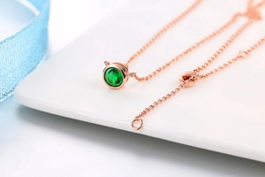 Macro del ciondolo in zircone verde con collana in oro rosa su un piatto bianco