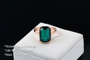 Detail of emerald-cut green crystal ring in 18K rose gold plating on a jewelry box