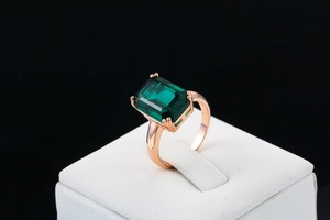 Detail of emerald cut green zircon ring with rose gold plating on a jewelry stand