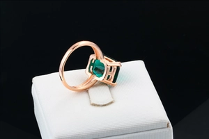 Macro view of emerald-cut green gemstone ring set in rose gold with a white jewelry box