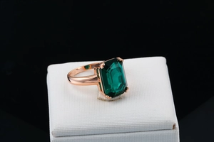 Close-up of emerald cut green gemstone ring with rose gold plating on a jewelry box