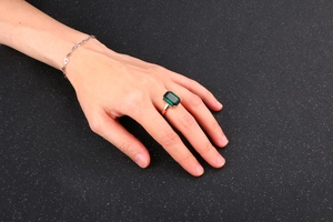 Detail of square emerald-cut green gemstone ring with a gold band and zircon accents