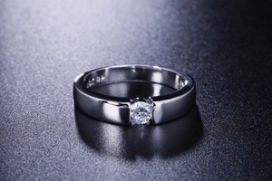 Macro shot of silver wedding ring with G18K engraving and round cut solitaire diamond