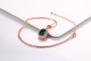 Dettaglio di una collana in oro rosa con gemma verde smeraldo e alone di diamanti bianchi