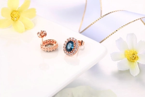 Dettaglio macro di orecchini halo con cristallo blu ovale e finitura in oro rosa e zirconi