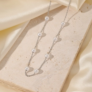 Elegante collar de acero inoxidable con 8 perlas redondas sobre fondo de piedra beige