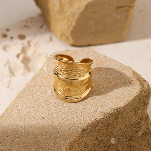 Irregular hammered wide open ring with gold plated finish on natural stone background