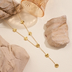 Barocke Y-Kette aus Titan mit 18k Gold Hammerschlag-Anhängern auf beigefarbenem Hintergrund