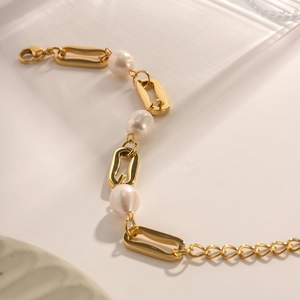 Elegant gold chain bracelet with rectangle links and pearls on a white tray