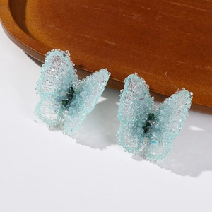 Detailed close-up of blue crystal butterfly earrings with green gem centers on wood