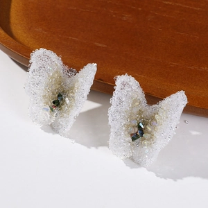 Macro detail of white translucent butterfly earrings with sparkling crystal textures