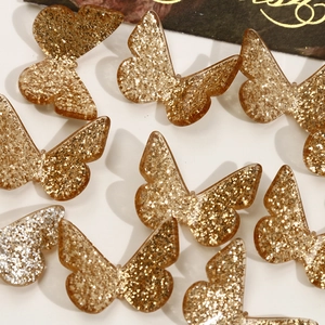 Flat lay of multiple golden glitter butterfly charms for DIY jewelry and hair accessories