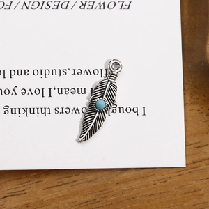 Vue détaillée d'un pendentif plume argentée vintage avec perle turquoise sur bois