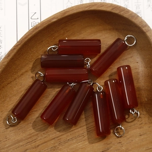 Macro shot of red agate cylinder pendants in a wooden bowl on calligraphy paper