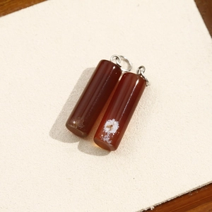 Macro shot of two cylindrical red agate stone charms with natural white veins for jewelry