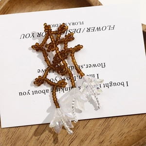 Dettaglio di perline marroni e fiori bianchi cangianti per accessori gioielli fai-da-te