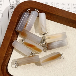 Detailed macro view of natural agate cylinder pendants with silver rings on wood tray