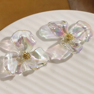 Iridescent acrylic three-petal flower earrings with golden core on a white ceramic tray