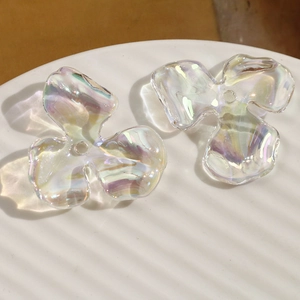 Macro shot of iridescent AB colored acrylic three-petal flower beads on a white tray