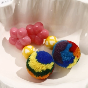 Close-up of DIY colorful plush ball earrings with pink resin flowers and heart beads