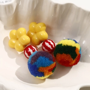 Handmade colorful pom-pom earrings with yellow flower studs on a white ceramic tray