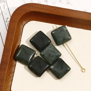 Macro detail van donkergroene vierkante jade kralen met gouden pin op houtvlak