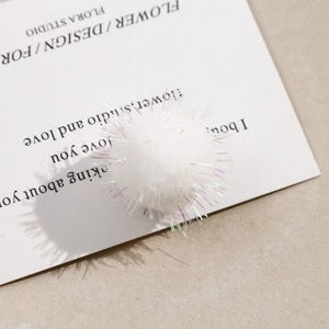 Macro shot of fluffy white pom-pom with colorful glitter threads for DIY hair accessories
