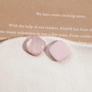 Close-up of pink square resin charms with pearlescent shell texture on a white ceramic tray