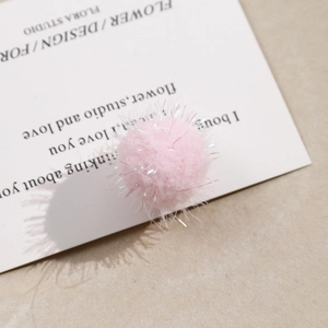 Macro view of a soft pink plush pompom with glittery fibers on a white display card