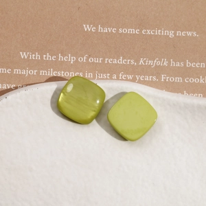 Close-up of olive green square resin stud earrings on a minimalist white ceramic tray