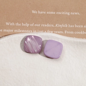 Close-up of square purple resin ear studs with pearlescent and matte texture detail